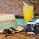 gray and black dslr camera beside sun hat and sunglasses